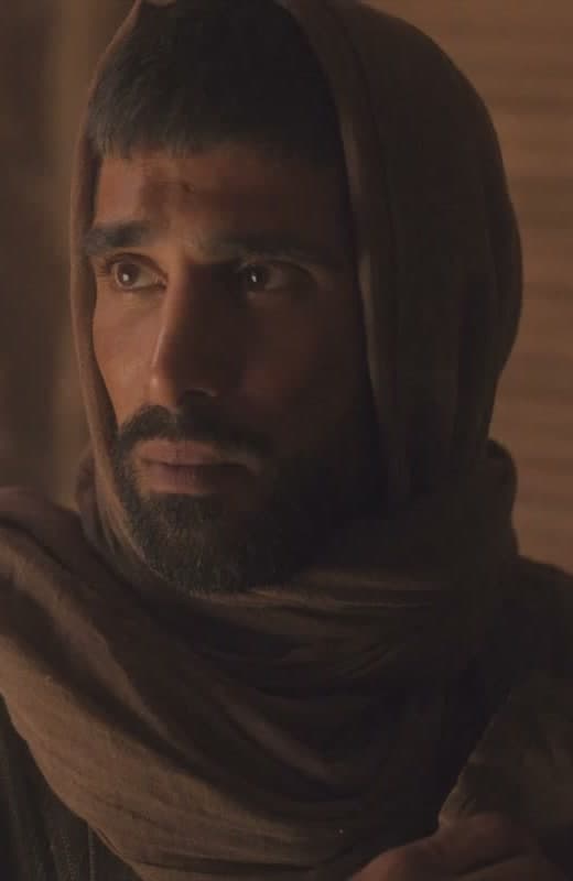 Dismas, hooded and pensive in warm candlelight — a still from the film